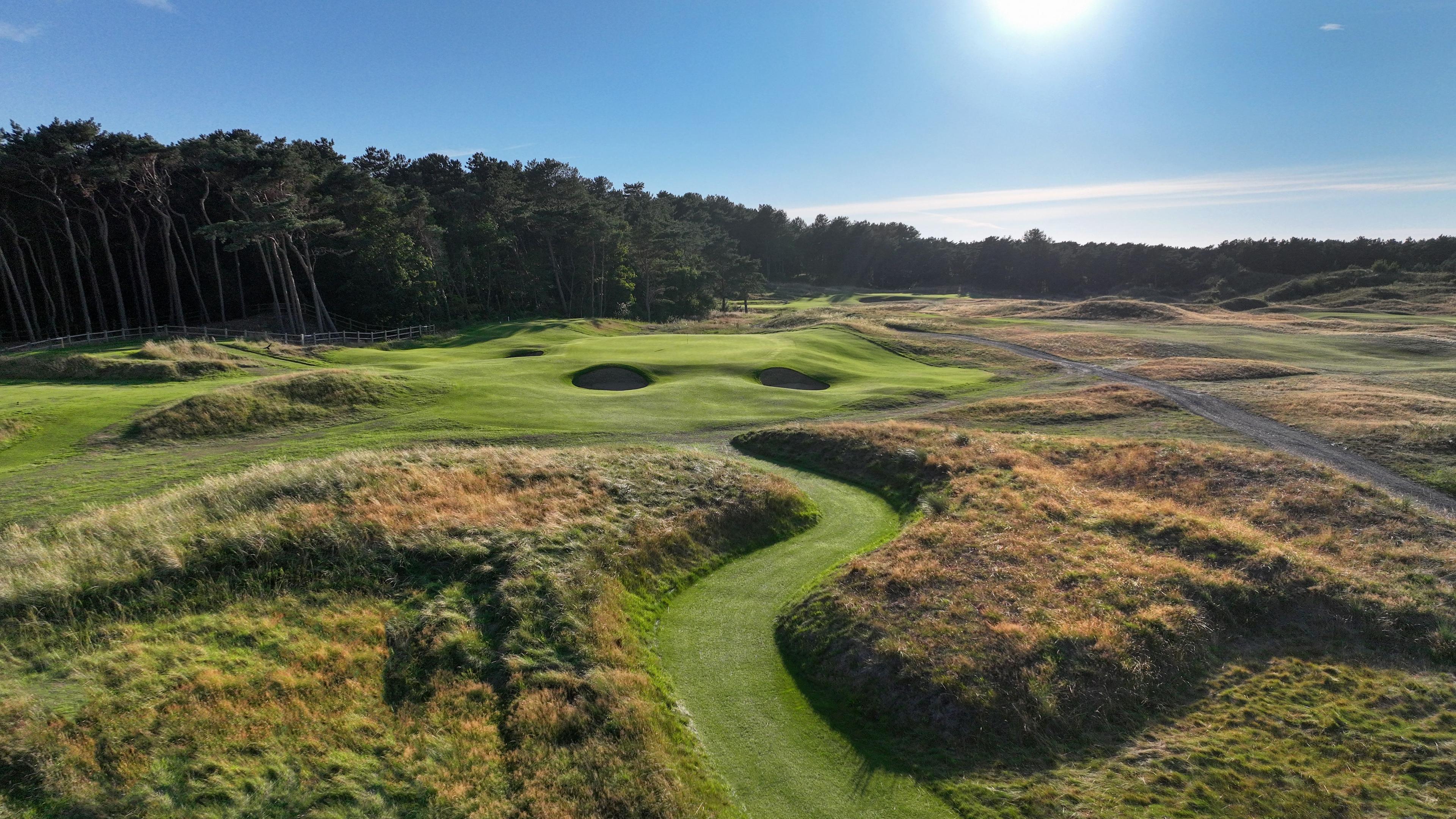 A winding fairway leads to a green surrounded by bunkers and tall pine trees.
