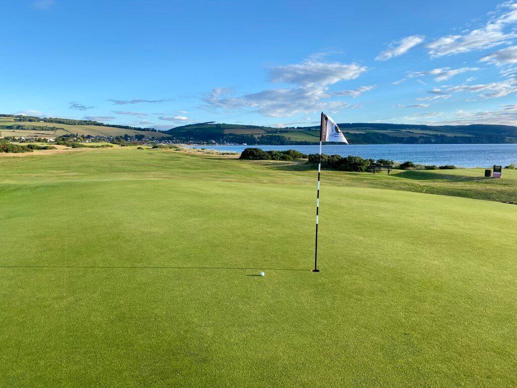 Close-up of a green overlooking the coastline and rolling hills.