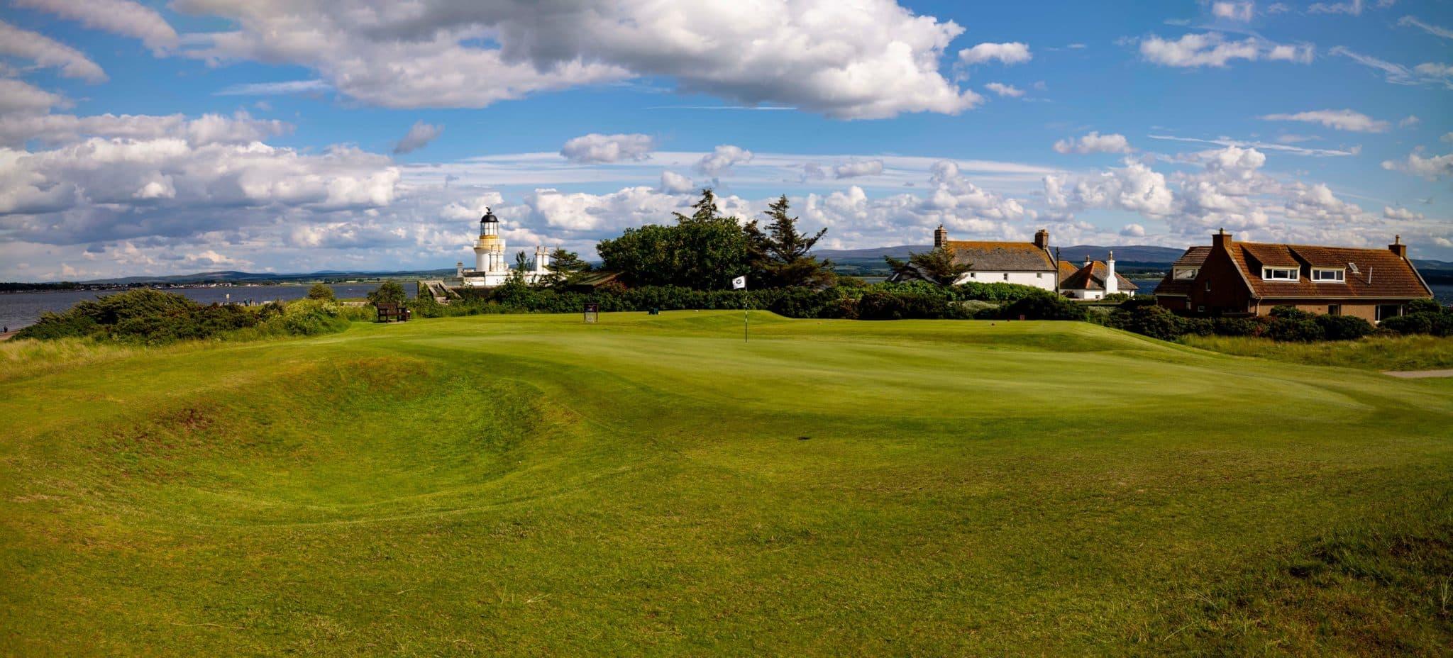 A picturesque green with a lighthouse and houses by the coastline.