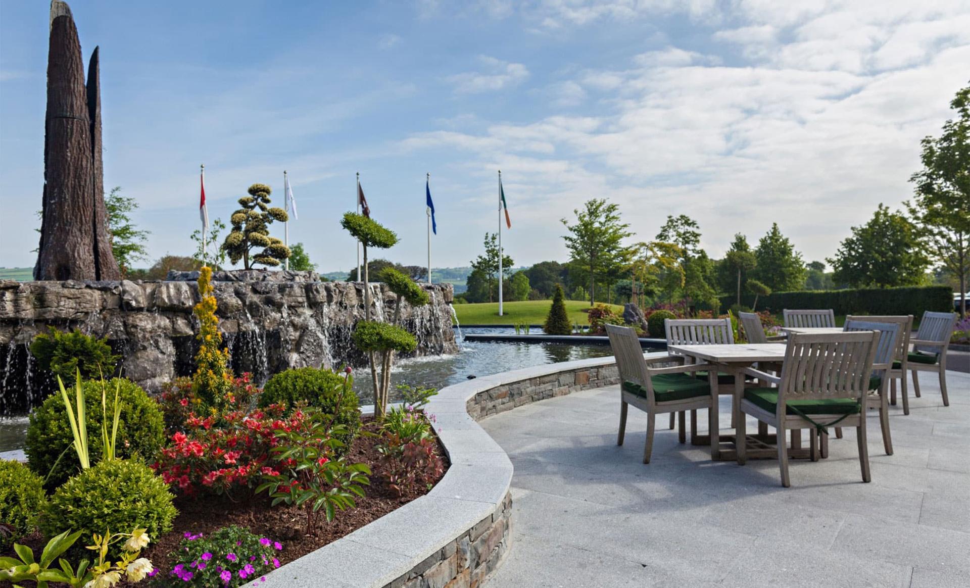 Outdoor seating beside a stone waterfall with vibrant gardens.