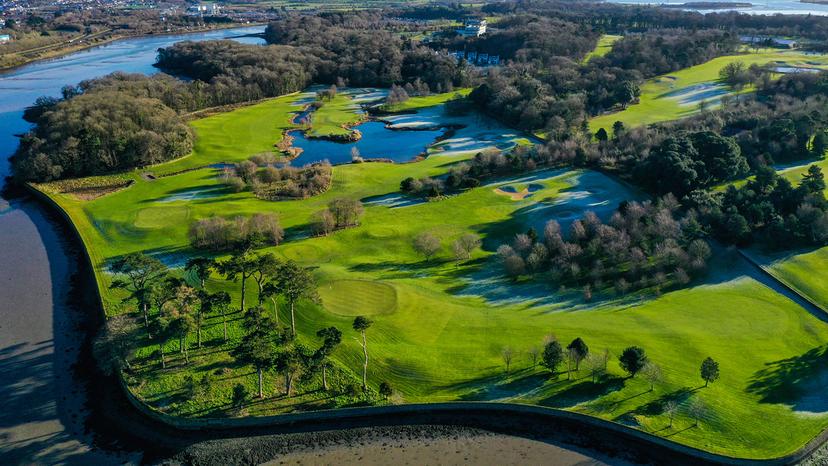 Aerial view of scenic golf course surrounded by water and woods.