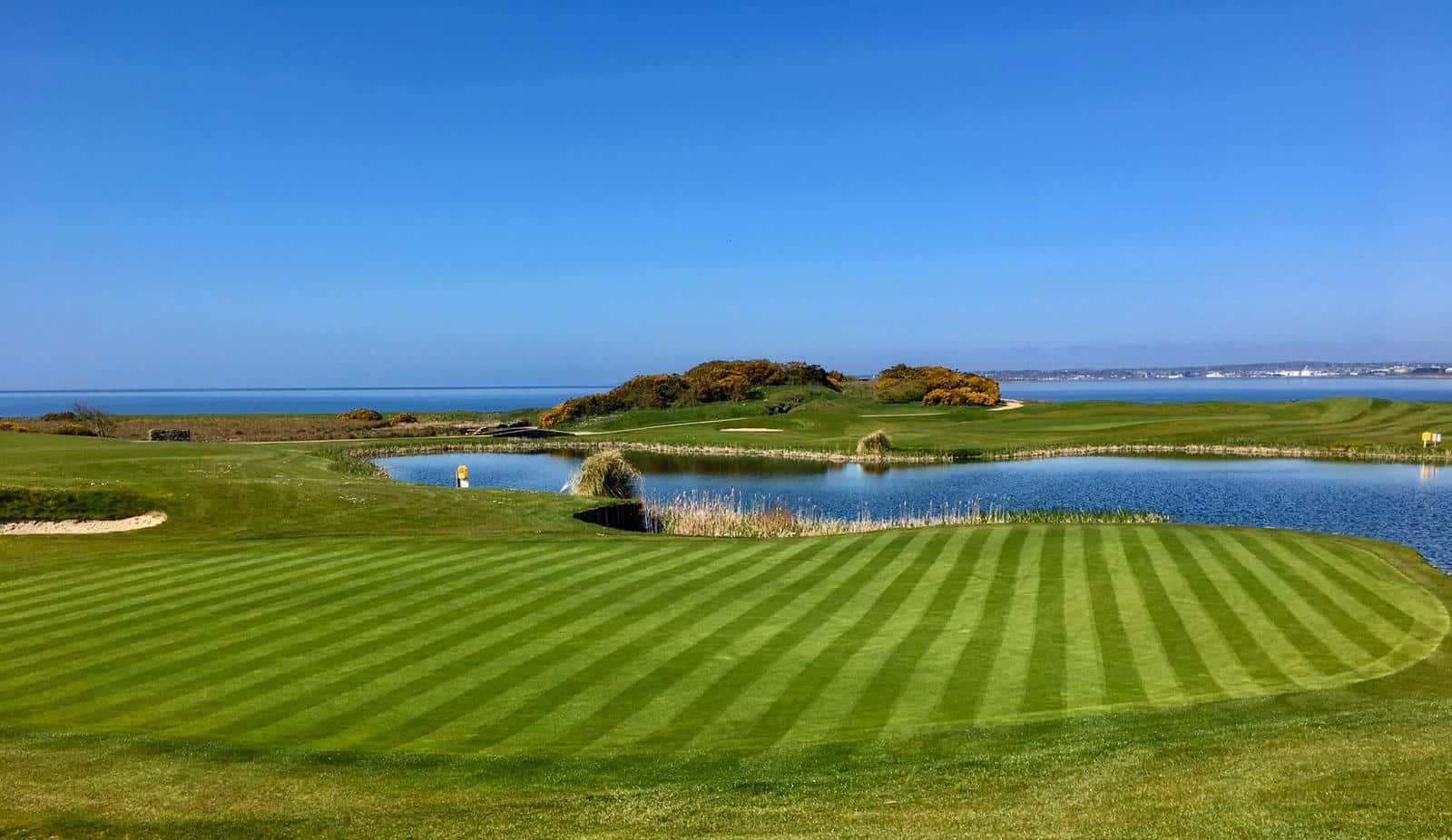 Wide view shot of well maintained greens with water features and a lovely view of the sea