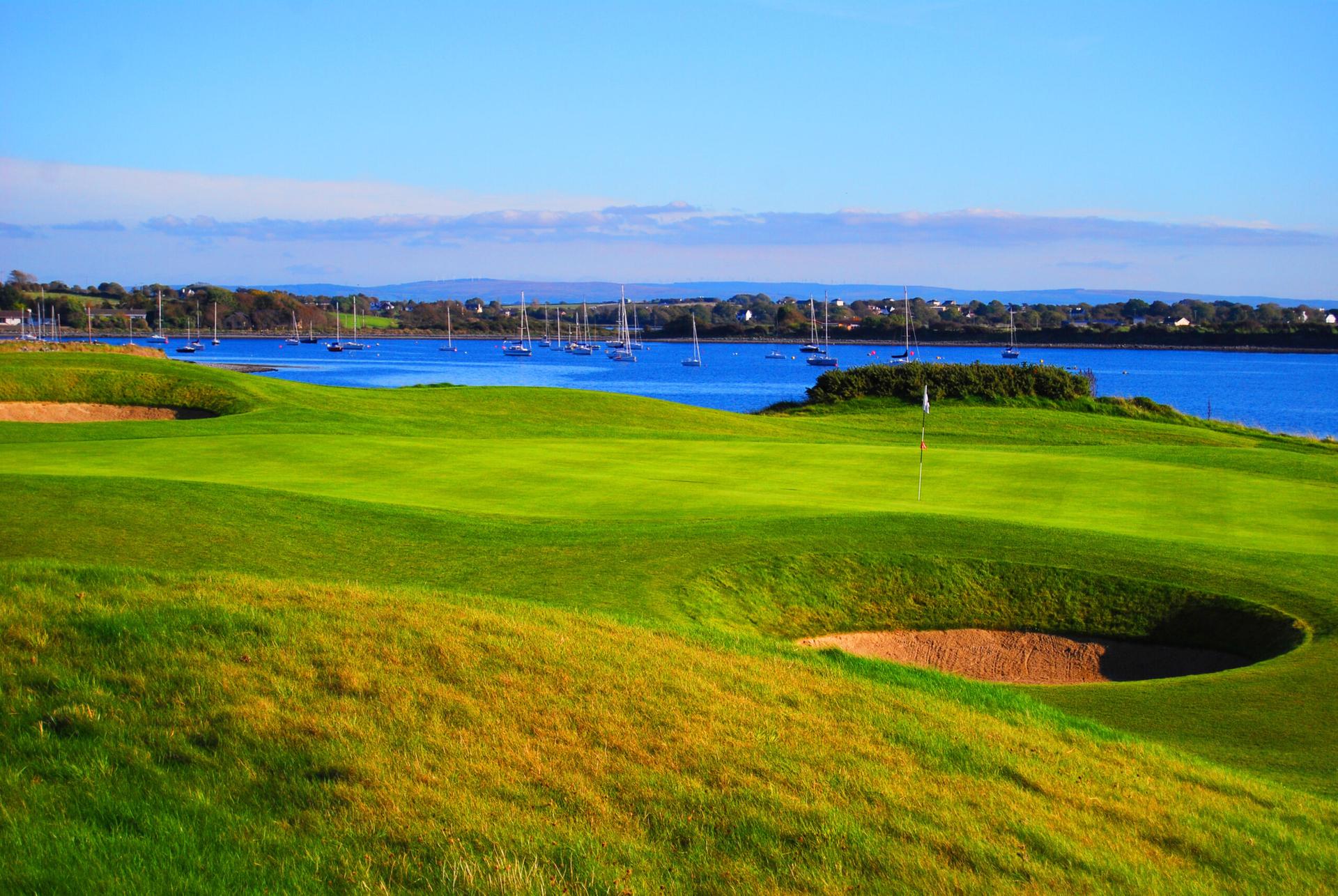 Putting greens surrounded by bunkers with multiple boats in the back in the sea