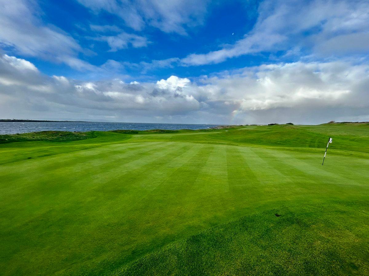Well-maintained greens on a cloudy day featuring a rainbow emerging in the background