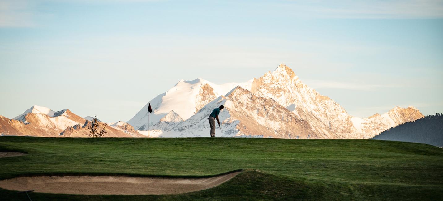 Golfer on putting green with a ice topped mountain in the distance