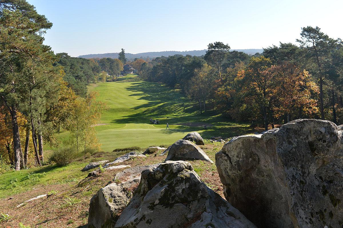 Tree-lined, undulating fairway leading up to the green, rocks in the foreground