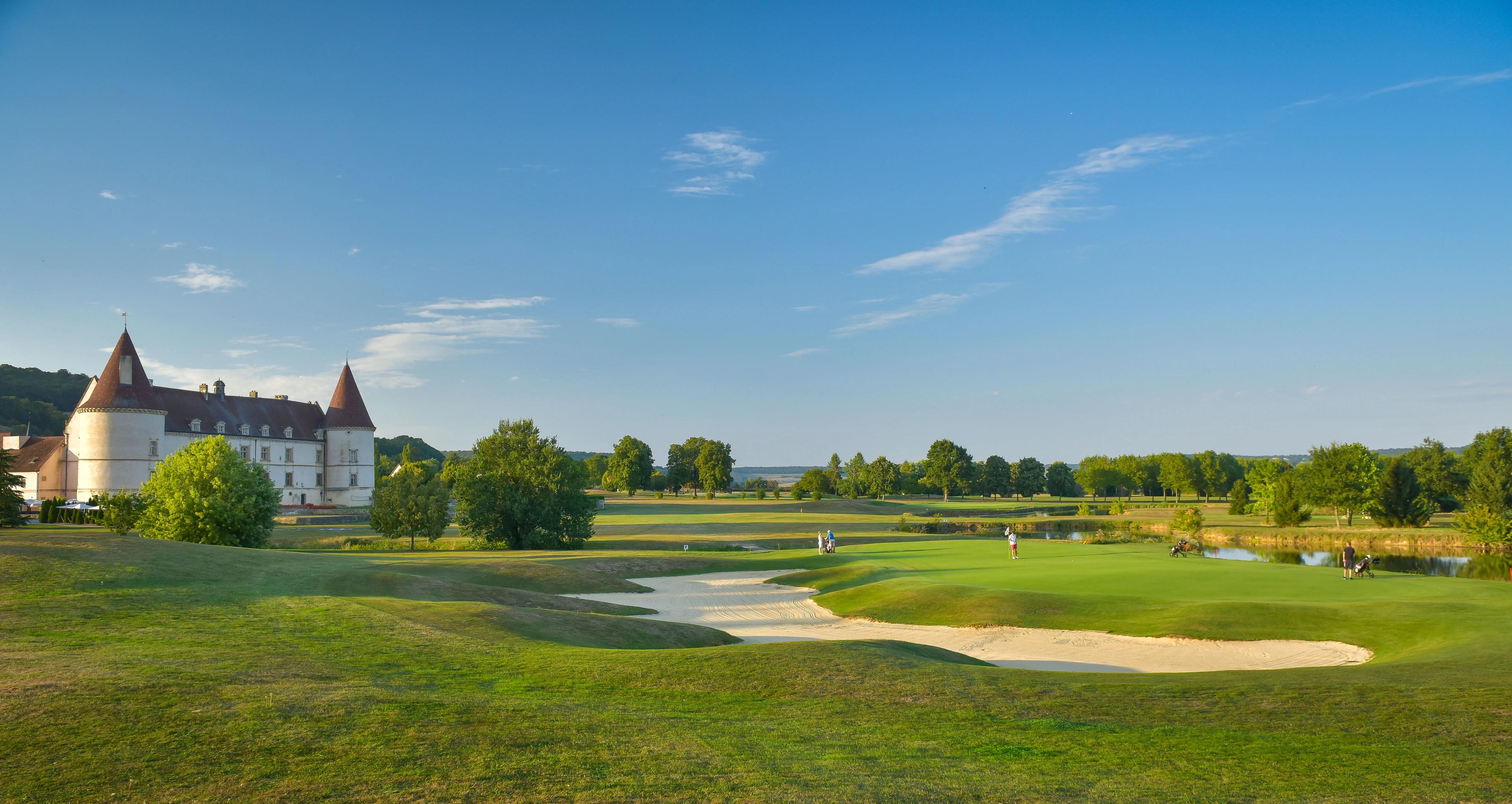 Wide view of the course with a large bunker surrounding a green with the hotel on the left