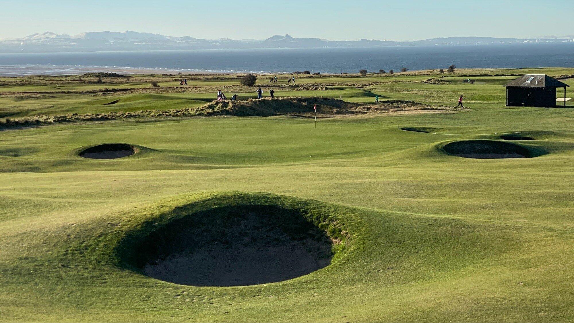 Deep sand bunkers strategically placed on the green with golfers enjoying their round under clear blue skies
