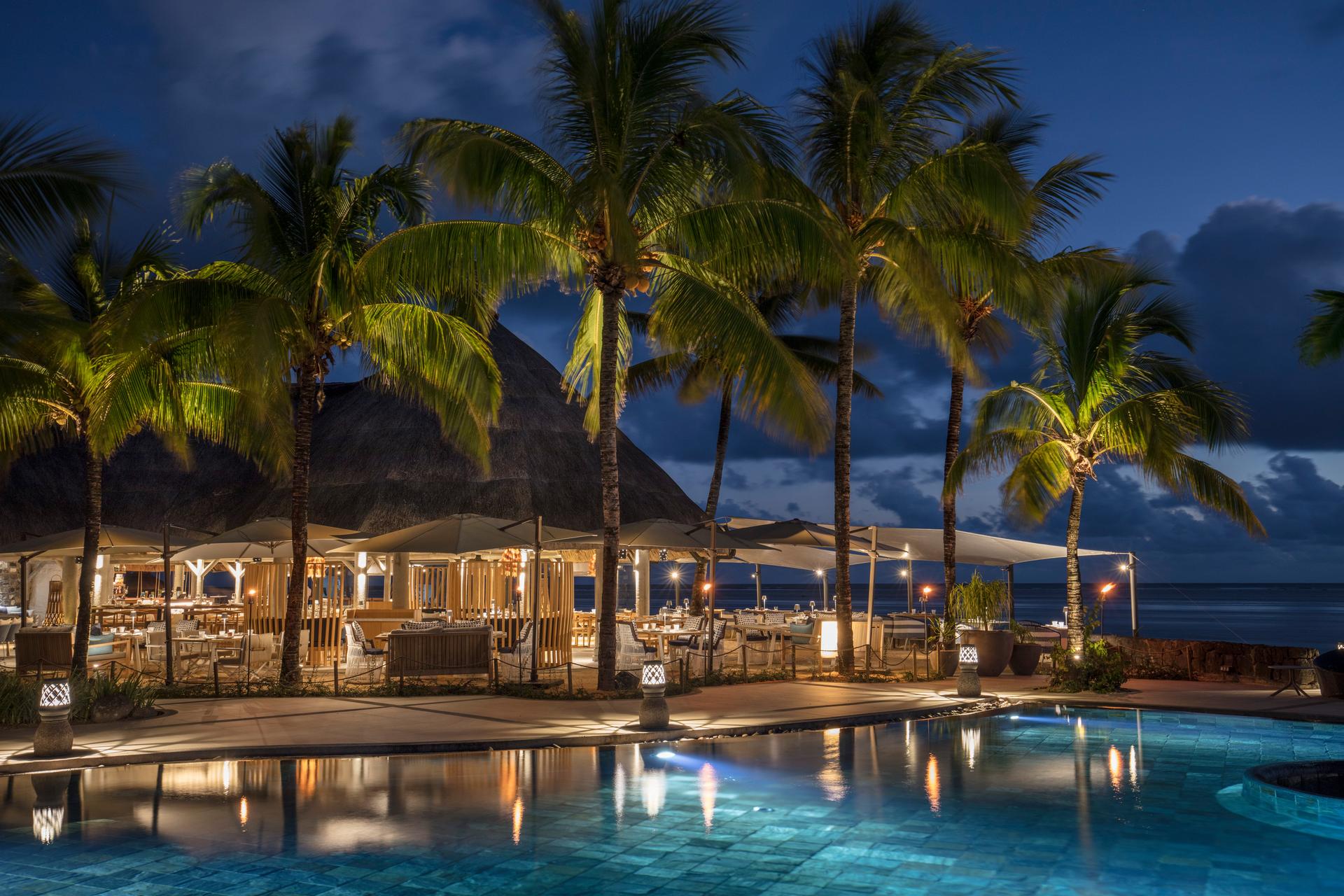 Poolside dining area framed by palm tree being lit up at night time