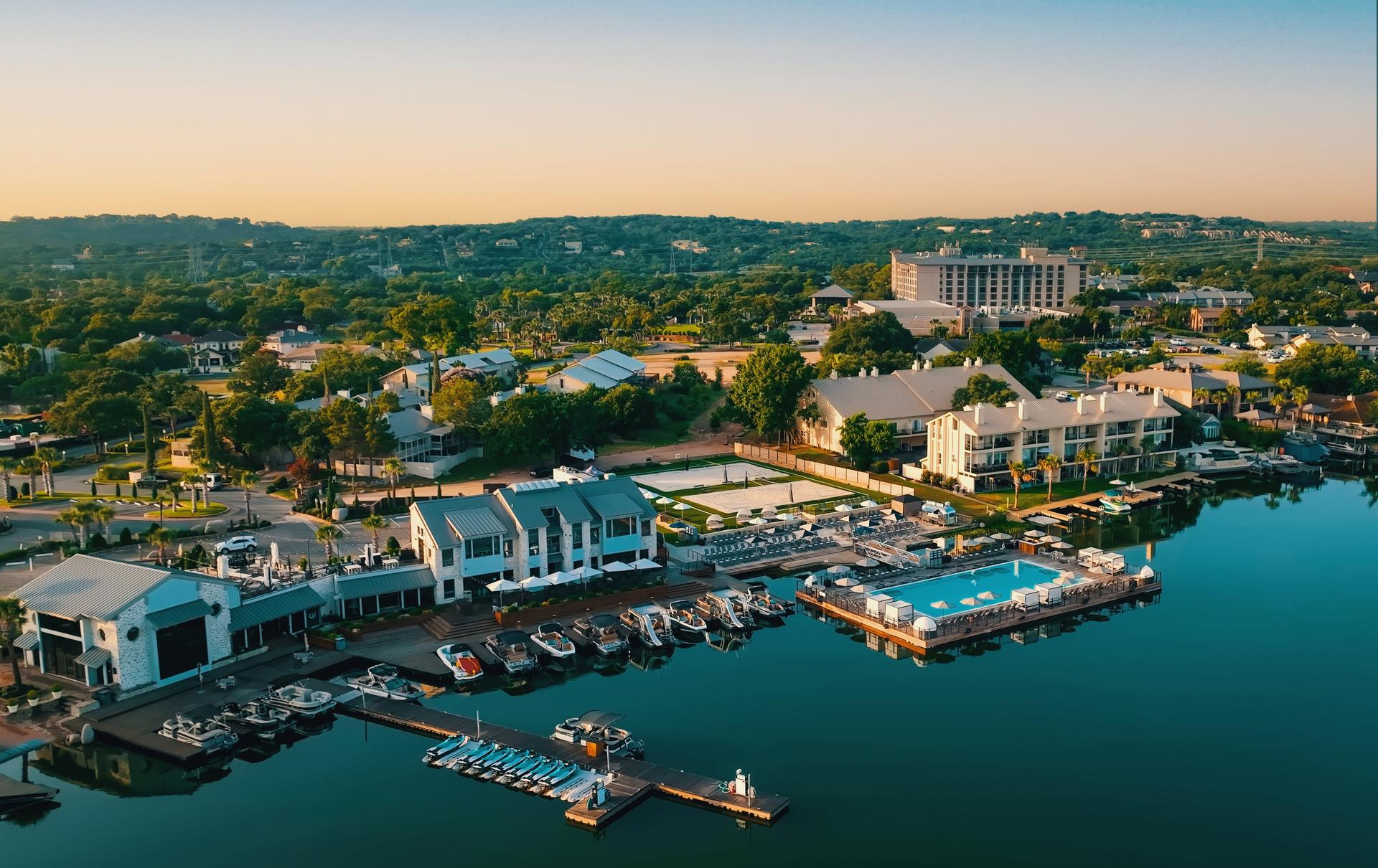 Boats docked beside a vibrant waterfront pool area, with calm waters reflecting the resort and hills.