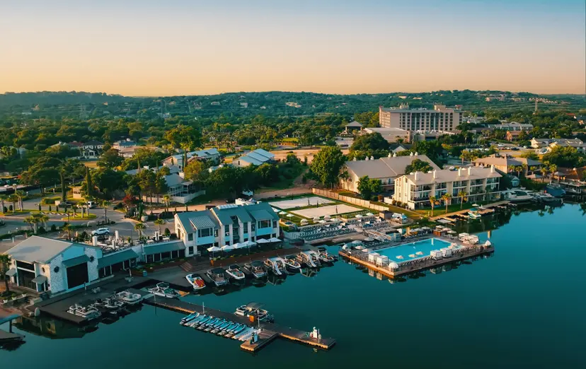 Boats docked beside a vibrant waterfront pool area, with calm waters reflecting the resort and hills.