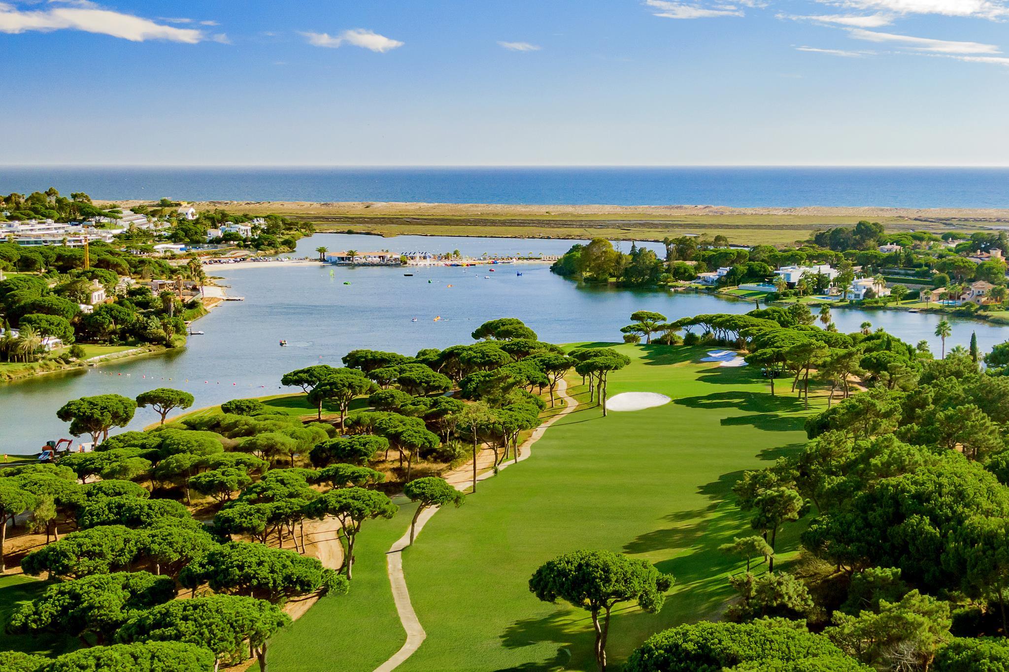 Aerial view of a tree-lined fairway leading to a green with water behind