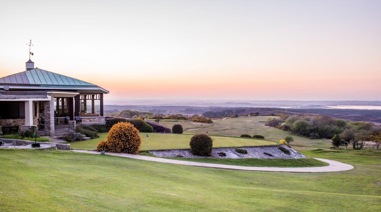 The Isle of Purbeck Golf Clubhouse looking over the course at sunset with practice putting green