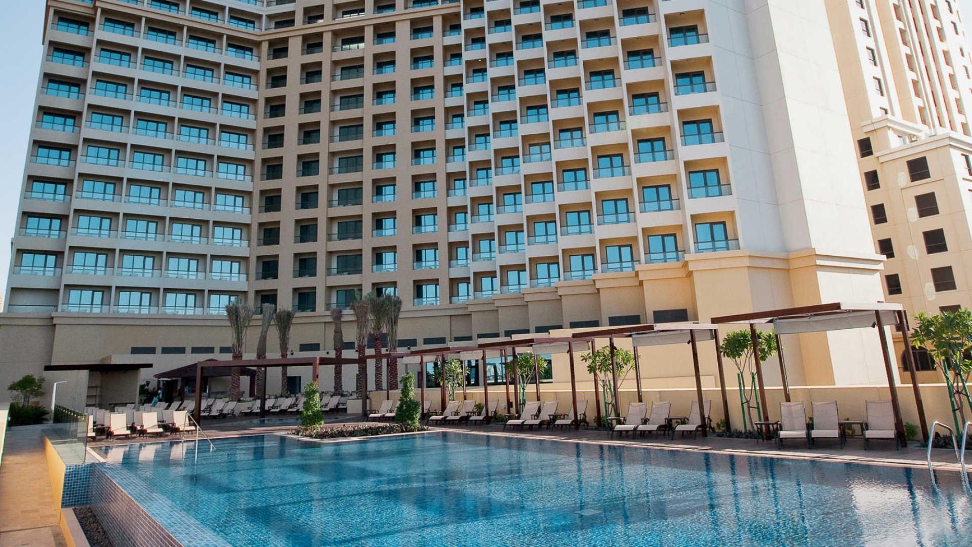 Outdoor swimming pool surrounded by sunbeds with the hotel building towering over