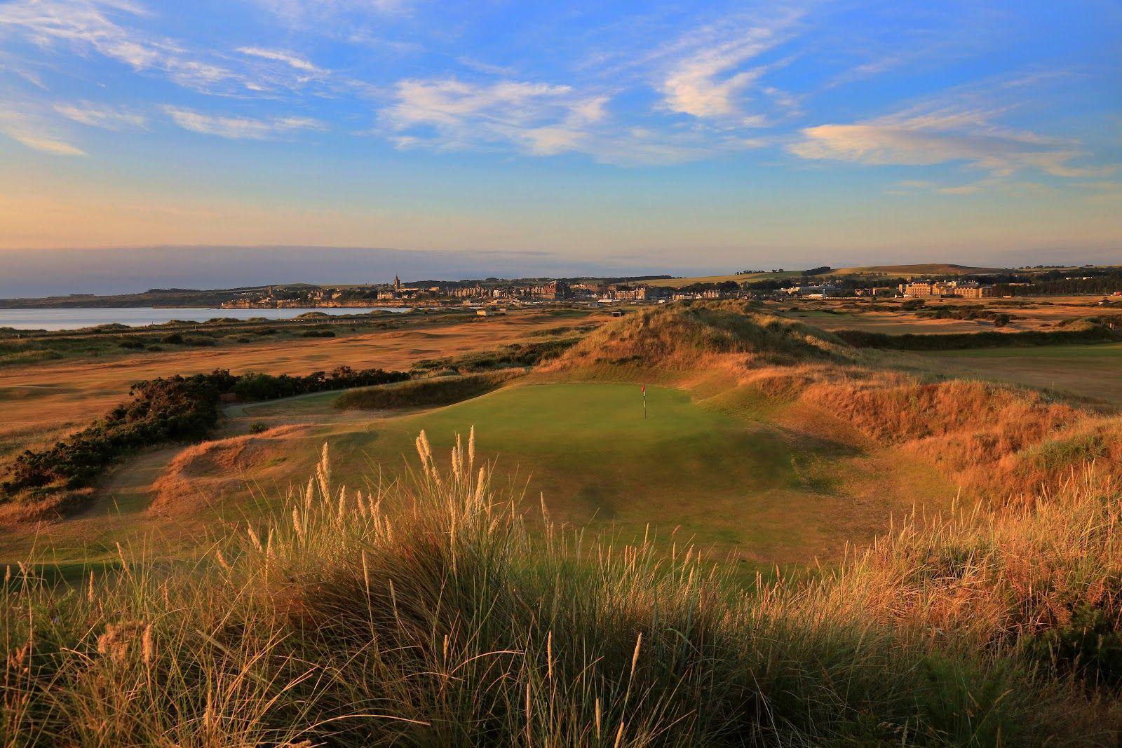 Sunset lighting up a green nestled among rugged dunes with views of the town beyond.