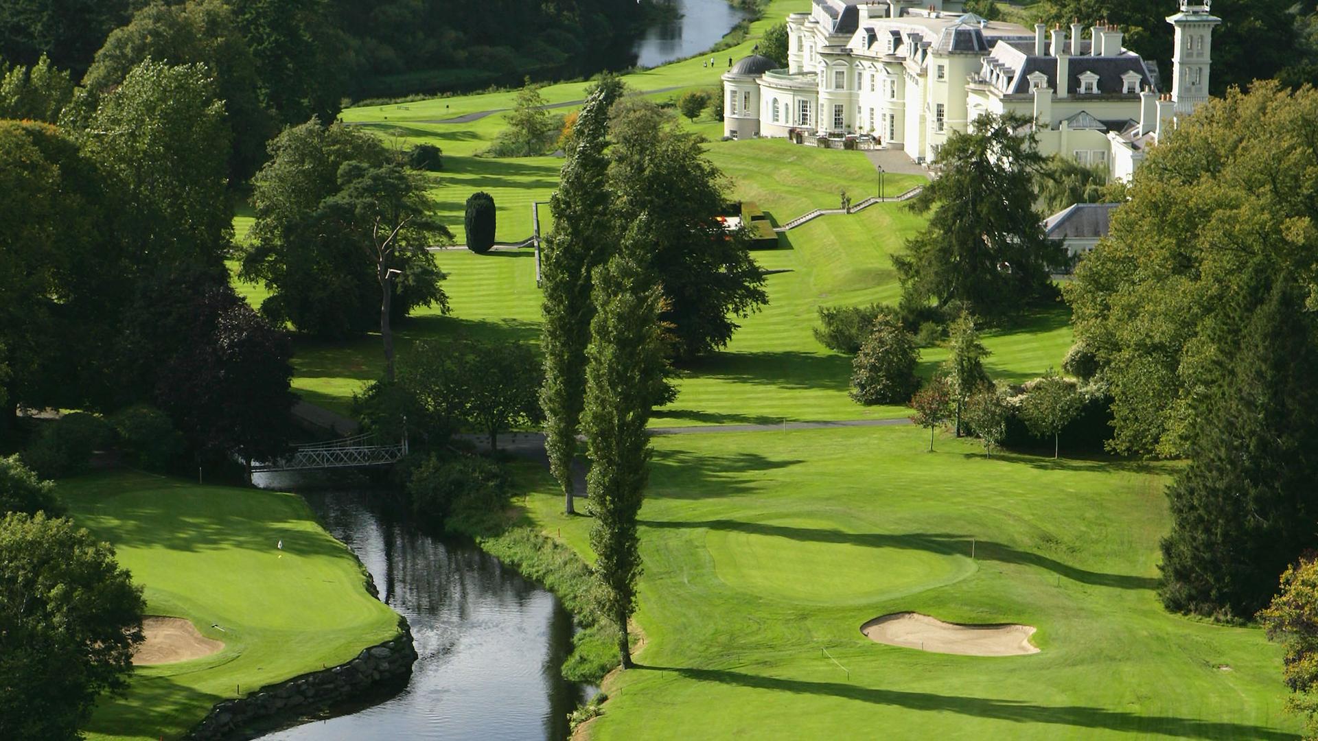 A majestic white mansion overlooking a scenic golf course with a winding river.