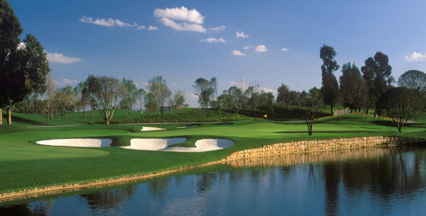 A picturesque golf hole with sand bunkers near a stone-edged water feature.