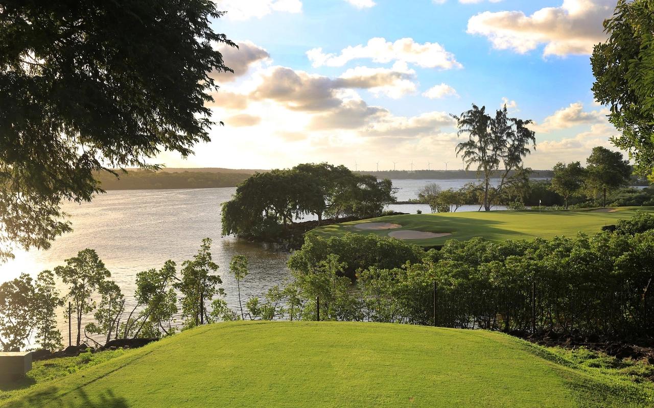 A scenic golf green by a calm lake during sunset.