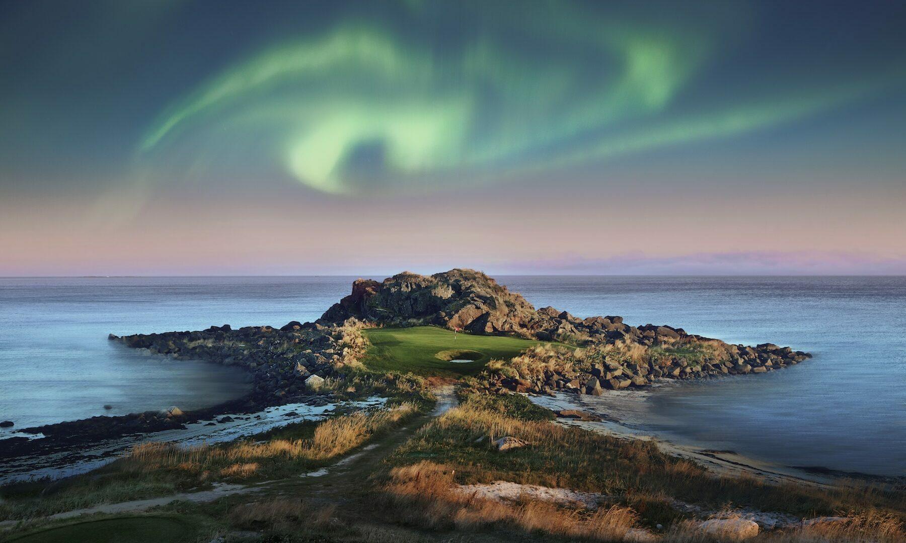 Northern lights over a island green surrounded by rocks before the ocean
