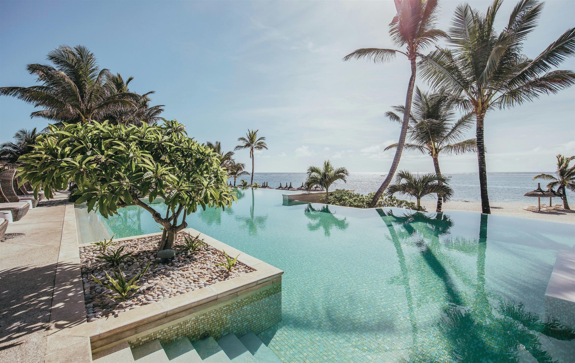 Sun shining down on the outdoor swimming pool with beach views causing it to reflect the surrounding palm trees