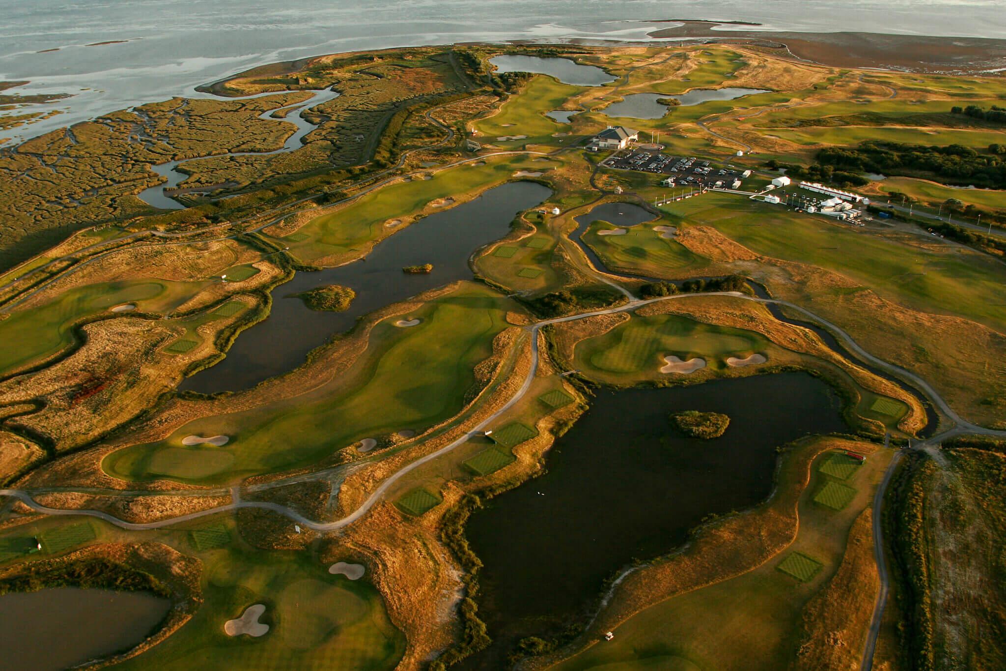 An aerial view of a golf course with winding fairways, water features, and a warm sunset glow.