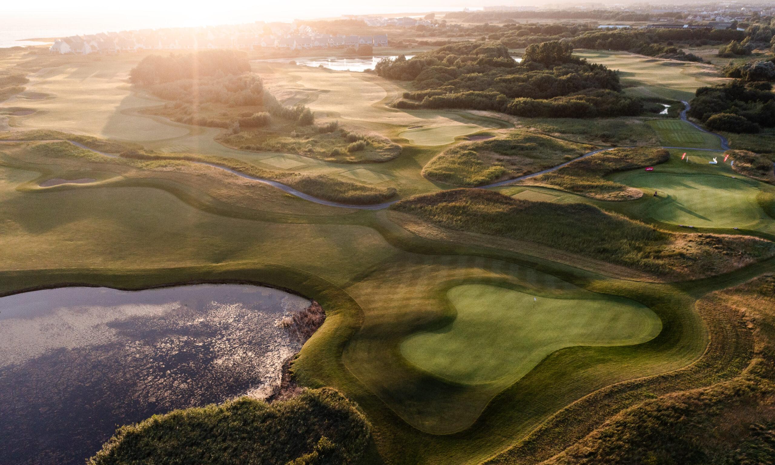 A vibrant golf course with well-maintained greens and a backdrop of trees and distant hills.