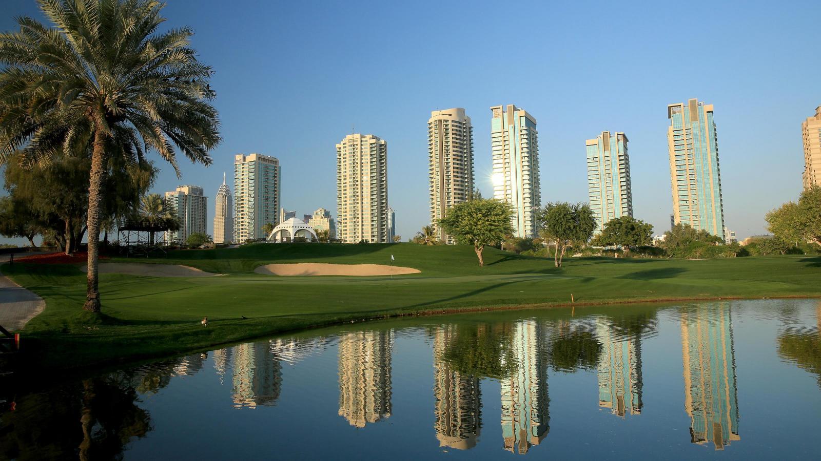 A smooth green sandwiched between sand bunkers and a water hazard reflecting the sky scrappers