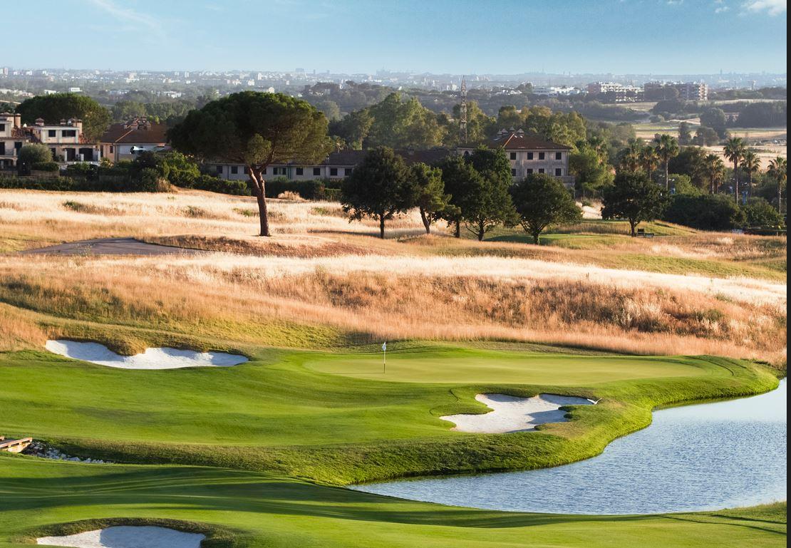 A downhill fairway leading to a smooth green surrounded by sand bunkers and a water hazard