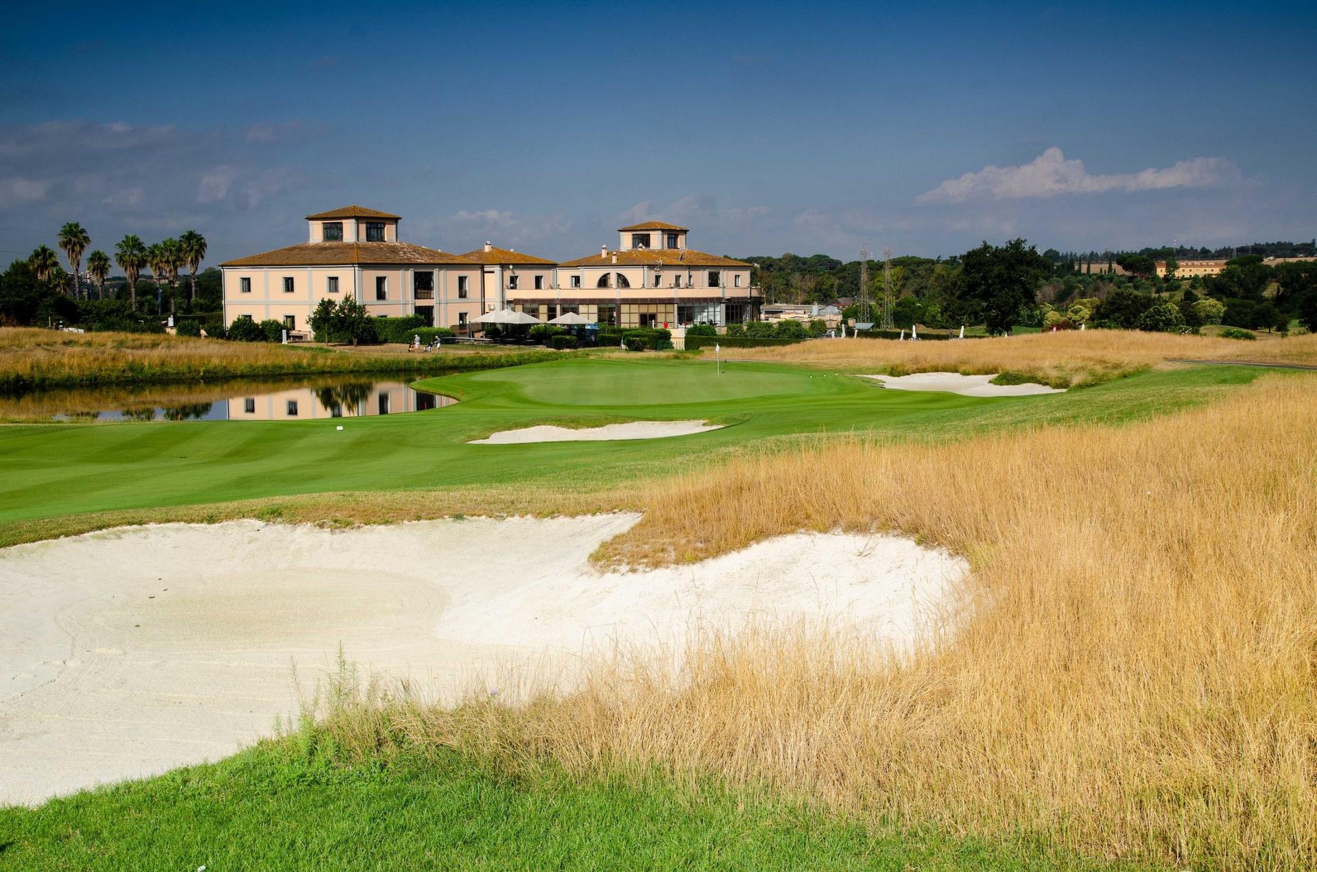 The Marco Simone Golf & Country Club clubhouse overlooking a smooth green sandwiched between a sand bunker and water hazard