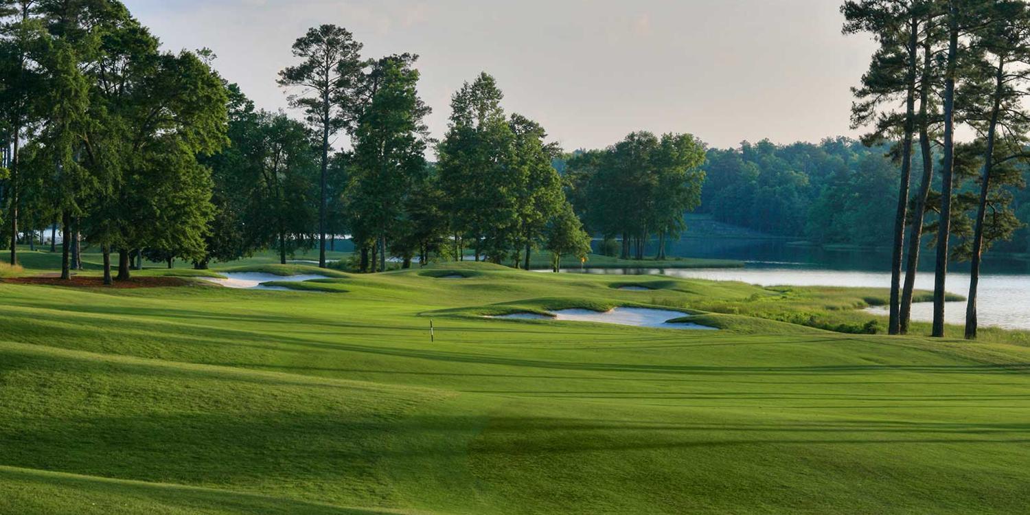 Panoramic view of a wide fairway leading to a smooth green nestled between sand bunkers and a water hazard