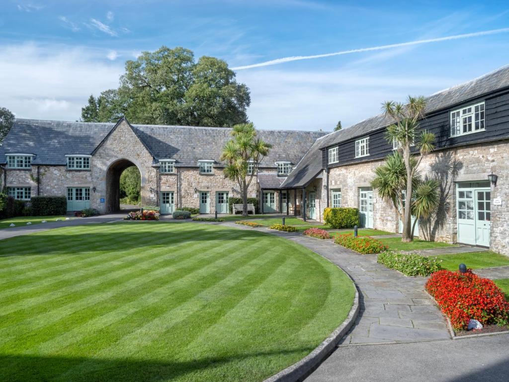 A historic stone building with an archway, set in a manicured lawn and trees.