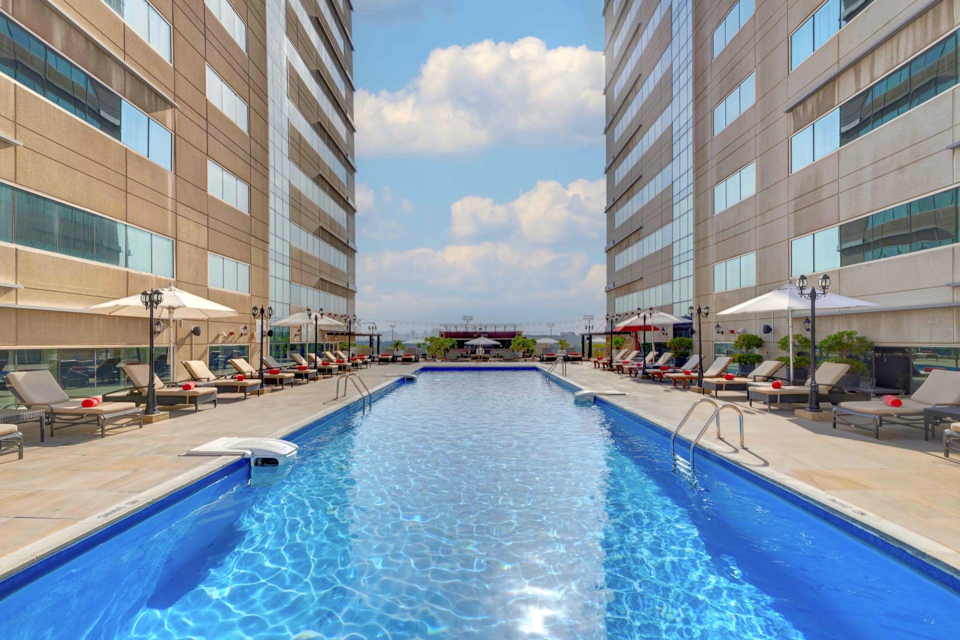 A swimming pool surrounded by sunbeds with distant city views