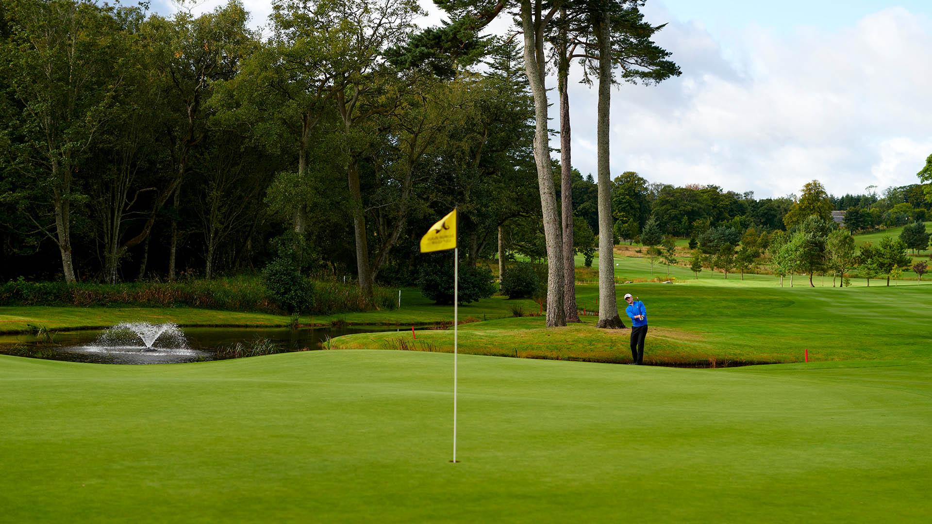 Golfer aiming for putting greens next to a water hazard on a cloudy day