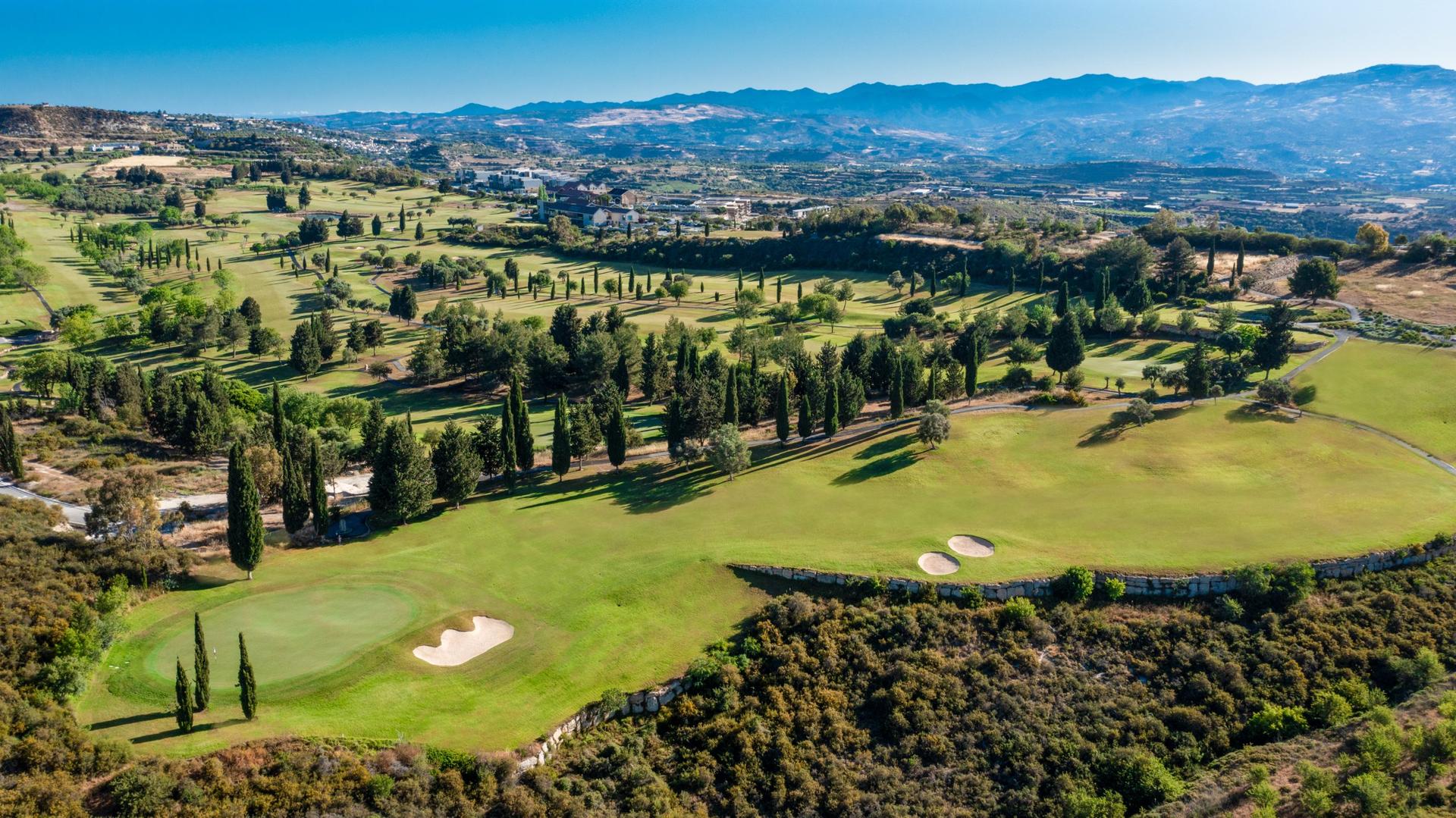 Aerial view of a wide fairway leading to a smooth green nestled with sand bunkers