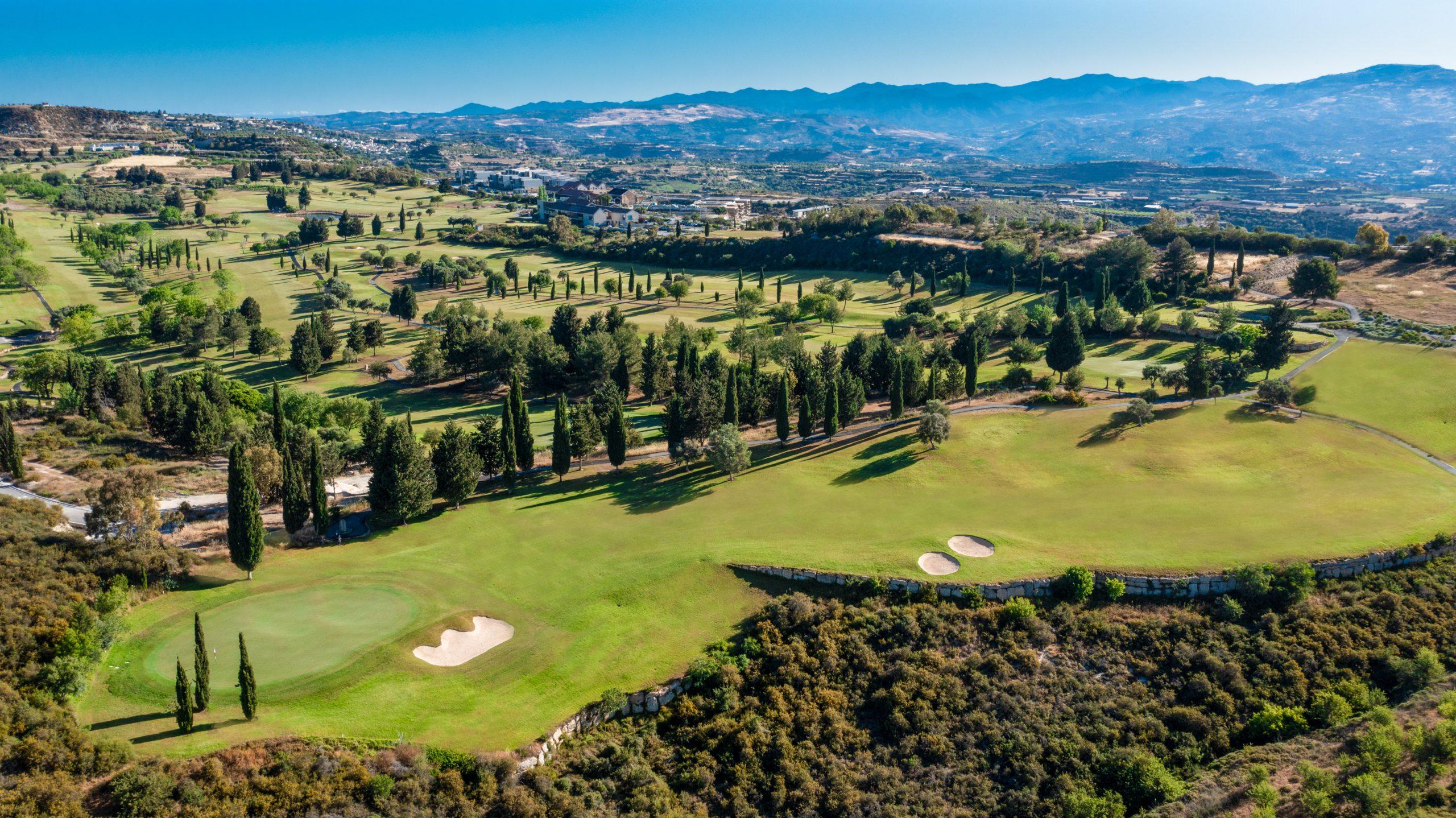 Aerial view of the course with rolling hills, tree-lined fairways, and bunkers blending into the landscape.