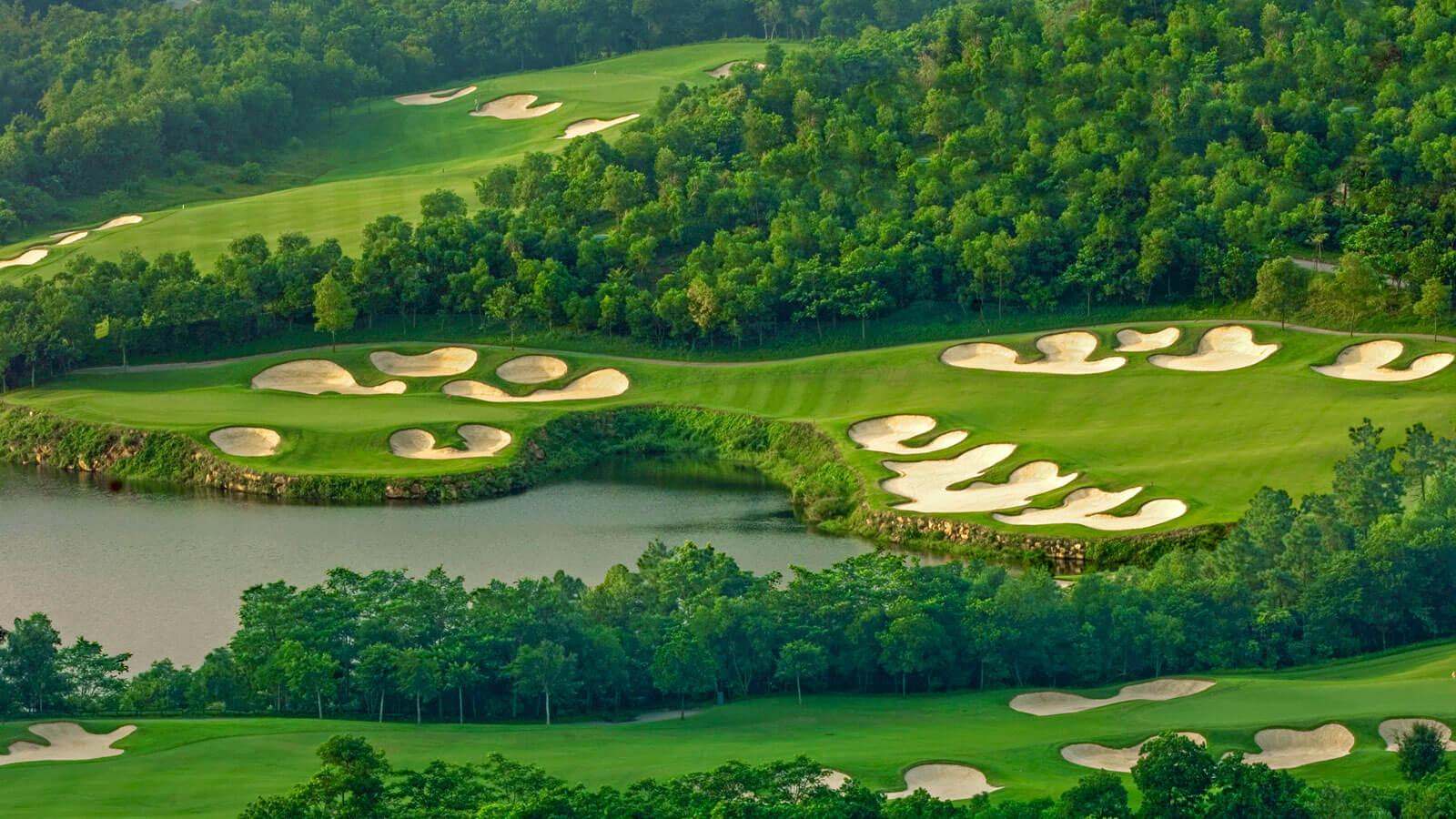 Aerial view of a lush golf course with multiple sand traps near a lake.