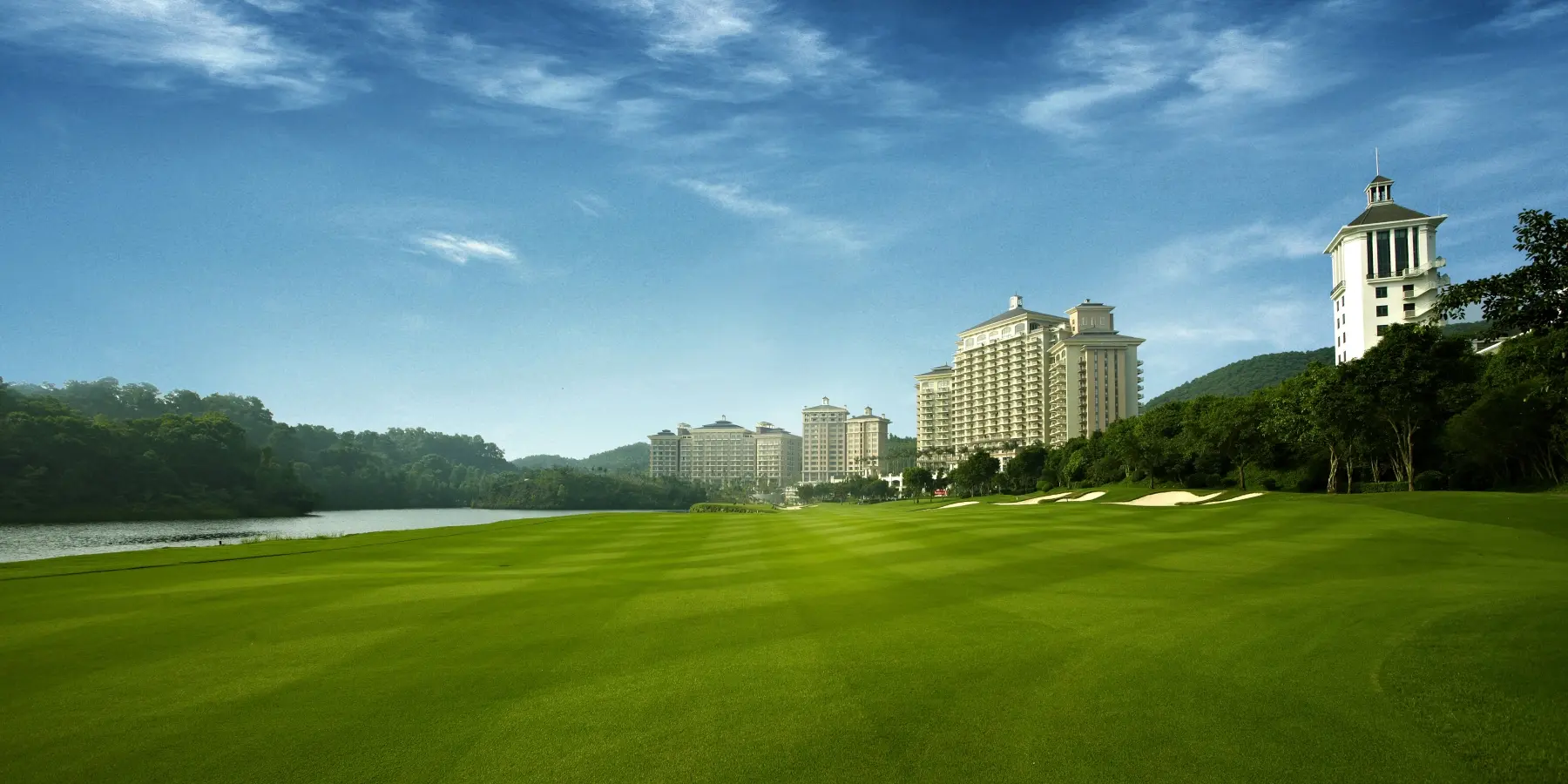A luxurious golf course with the grand Mission Hills Dongguan buildings in the background.