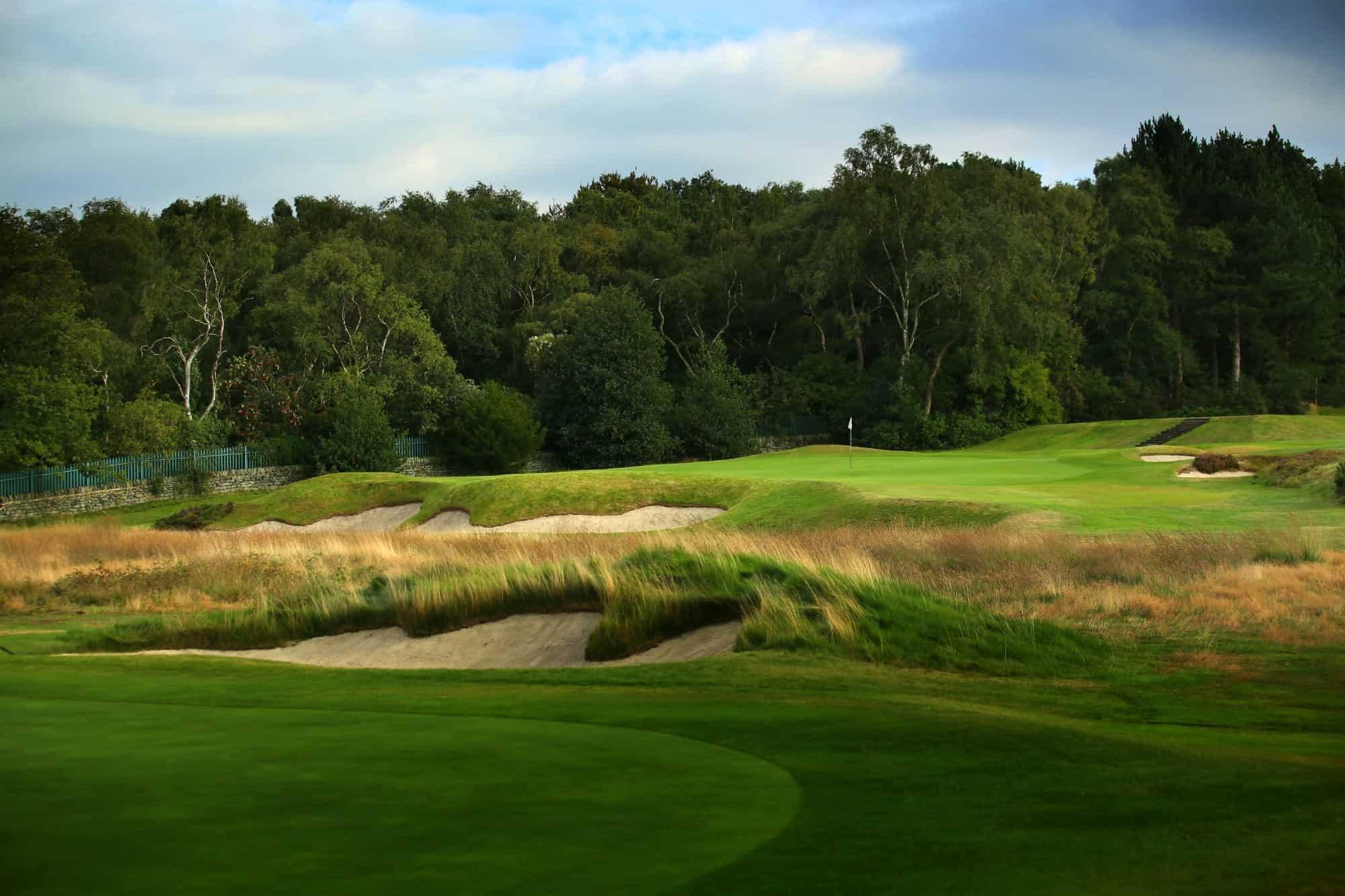 A golf hole with rugged bunkers, bordered by tall trees and natural rough.