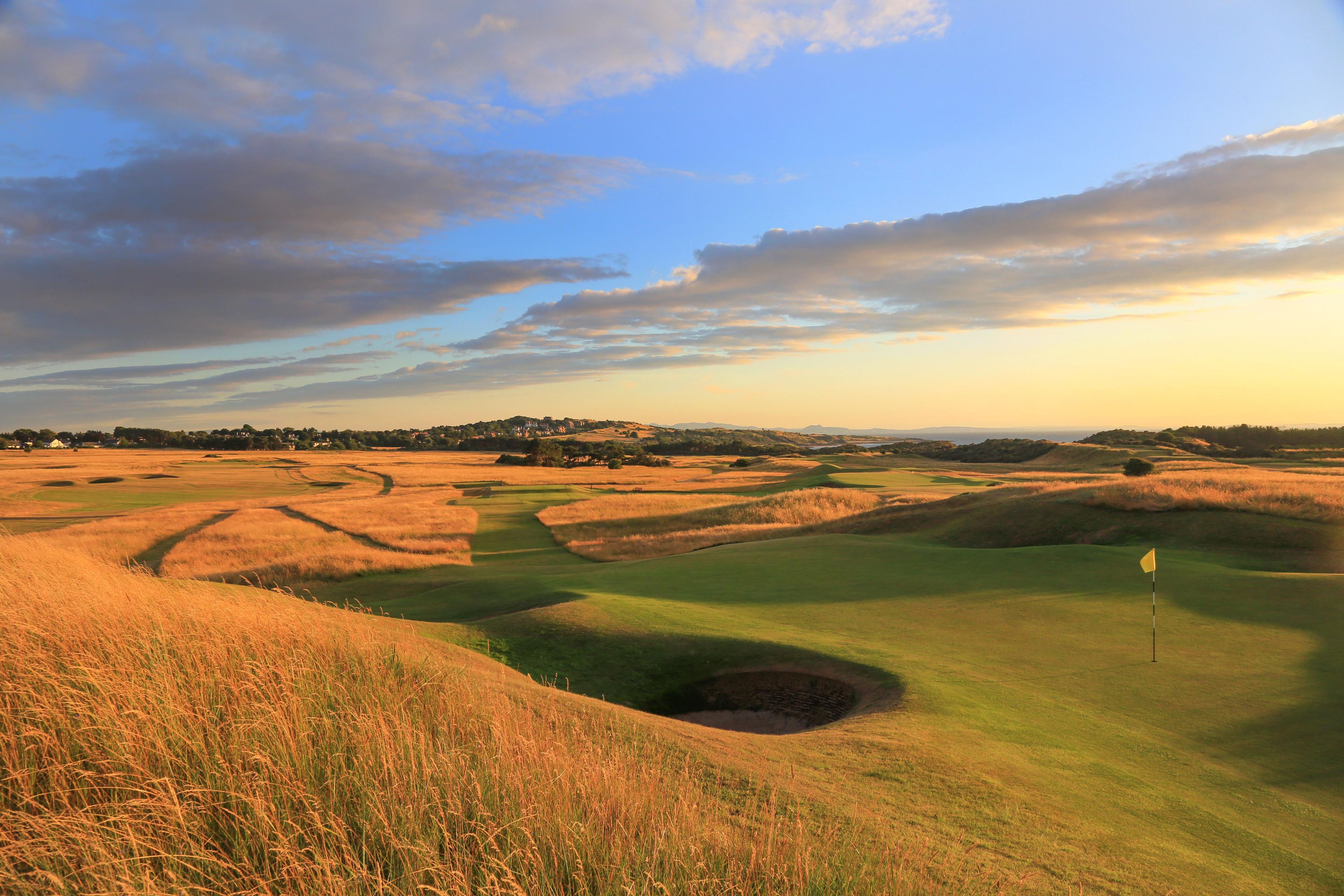 Panoramic view of the golden rough surrounding manicured green under blue skies during sunset