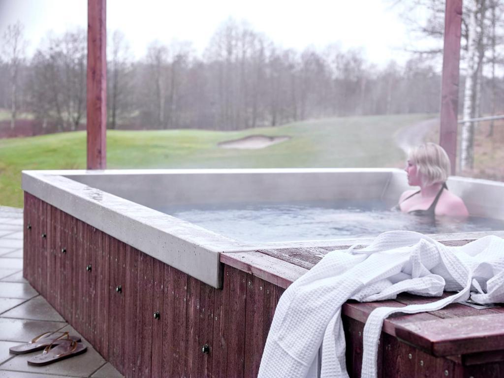 A person relaxing in a steaming hot tub overlooking a golf course on a misty day.