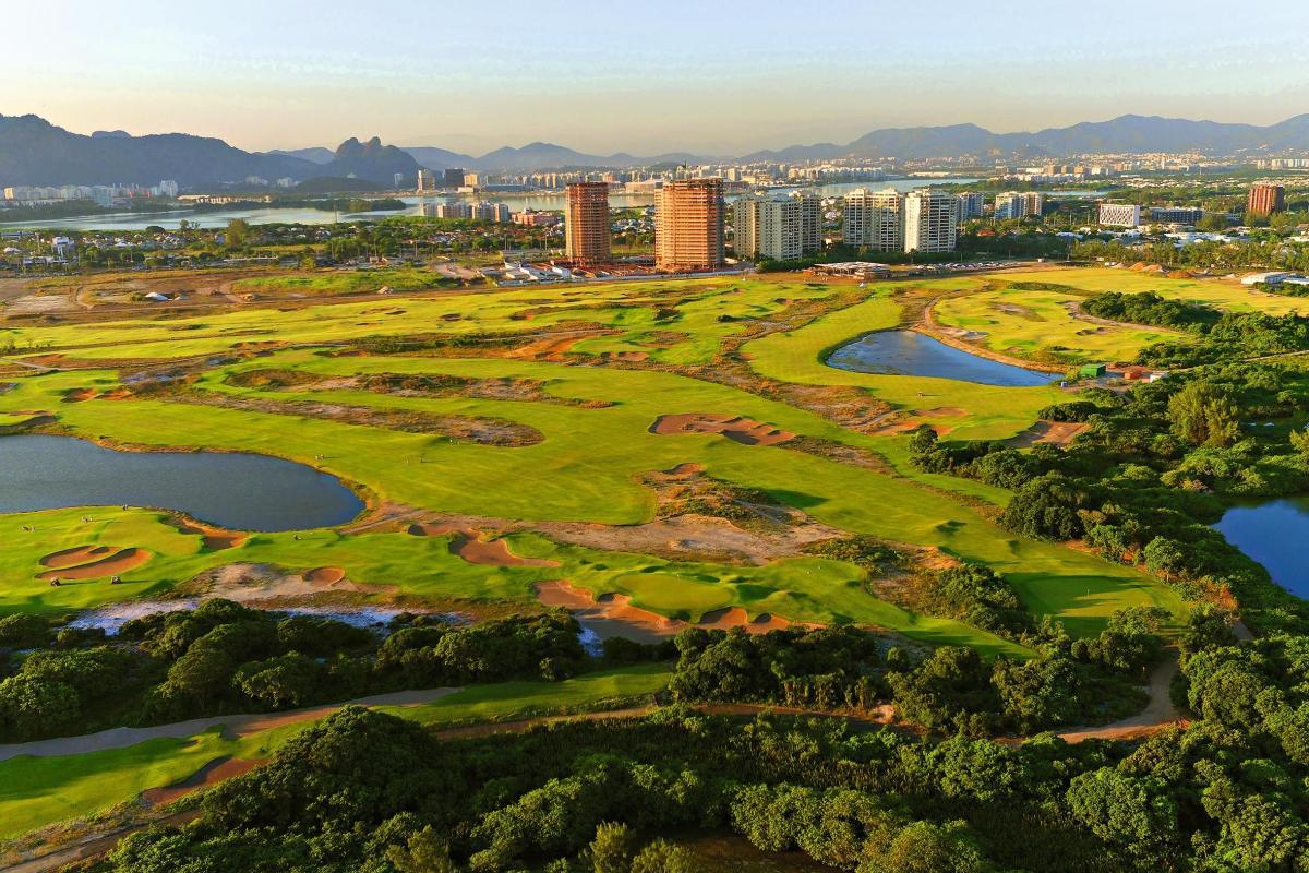 A wide view of a golf course surrounded by city buildings and natural landscapes