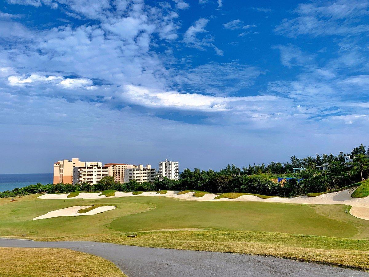 An extra large sand bunker surrounding a smooth green under cloudy blue skies