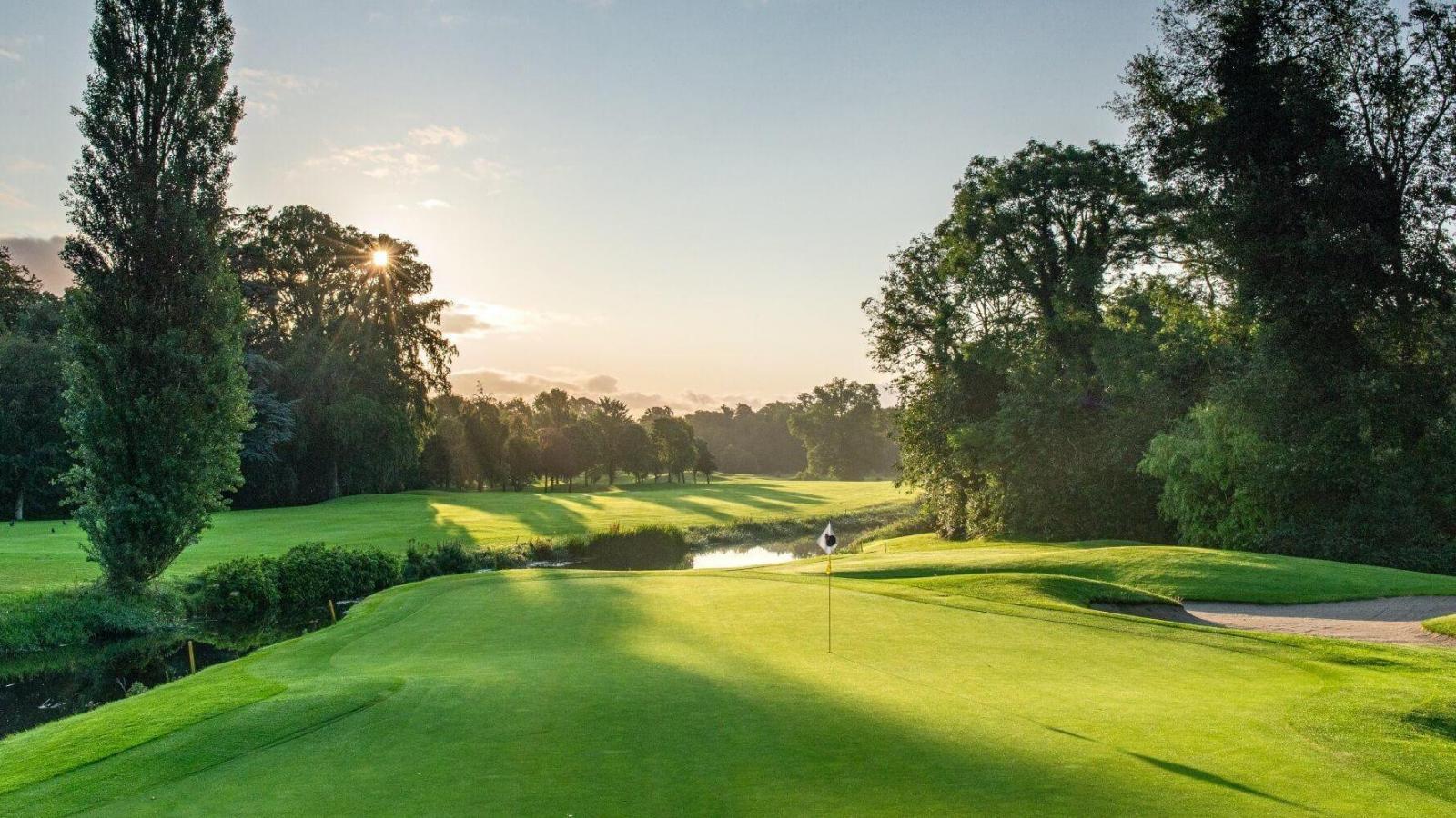 A peaceful golf green glows in the soft light of sunrise.