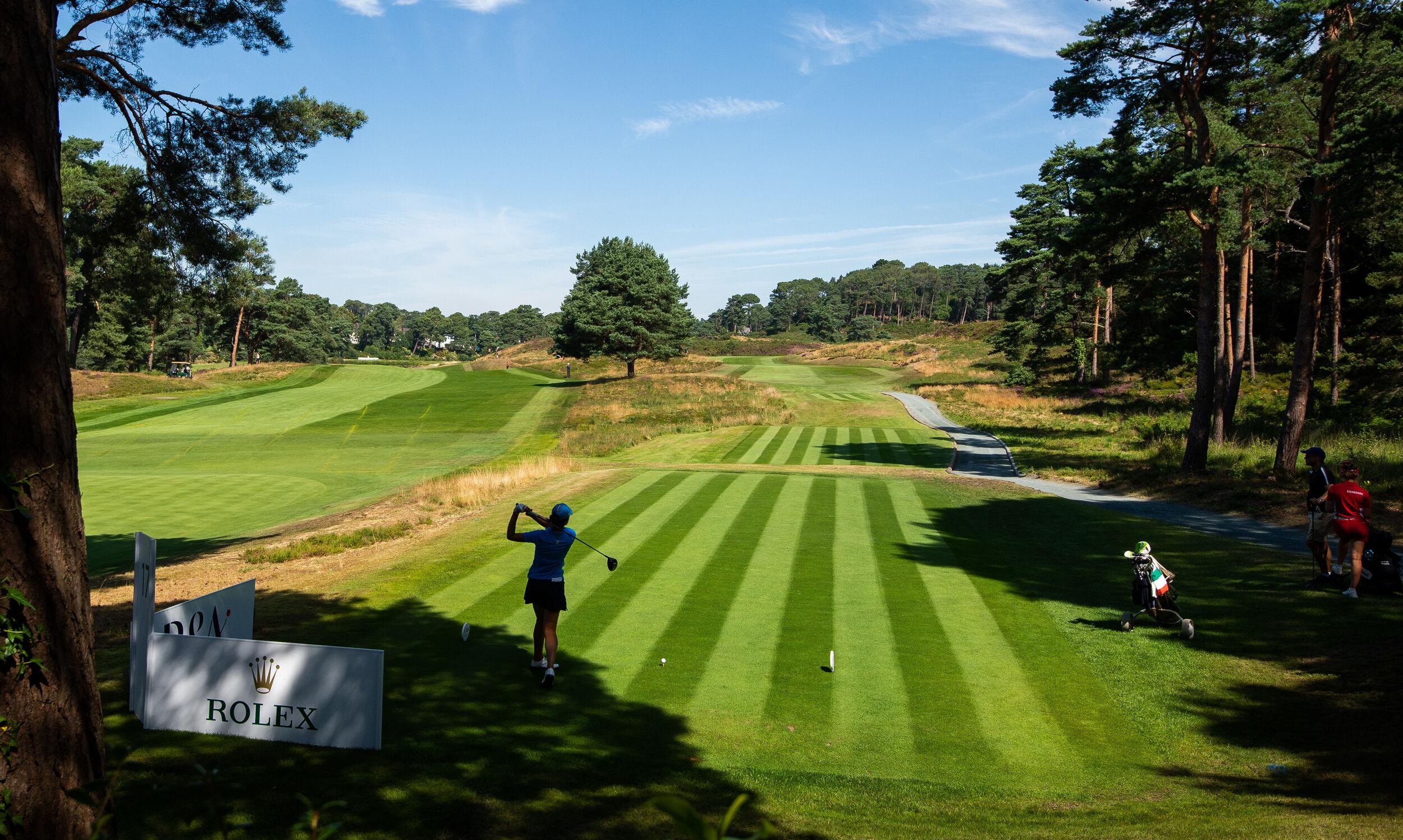 A golfer tees off on a perfectly striped fairway surrounded by trees.