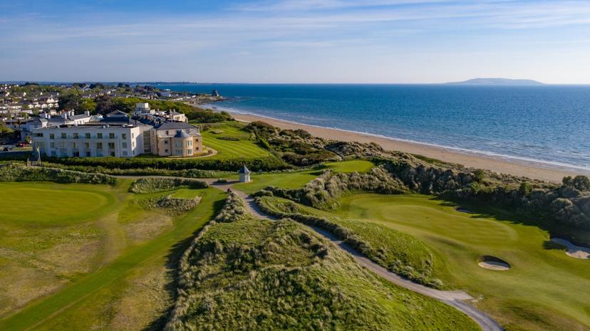 A resort sits beside a golf course and a sandy beach with the ocean stretching into the horizon.