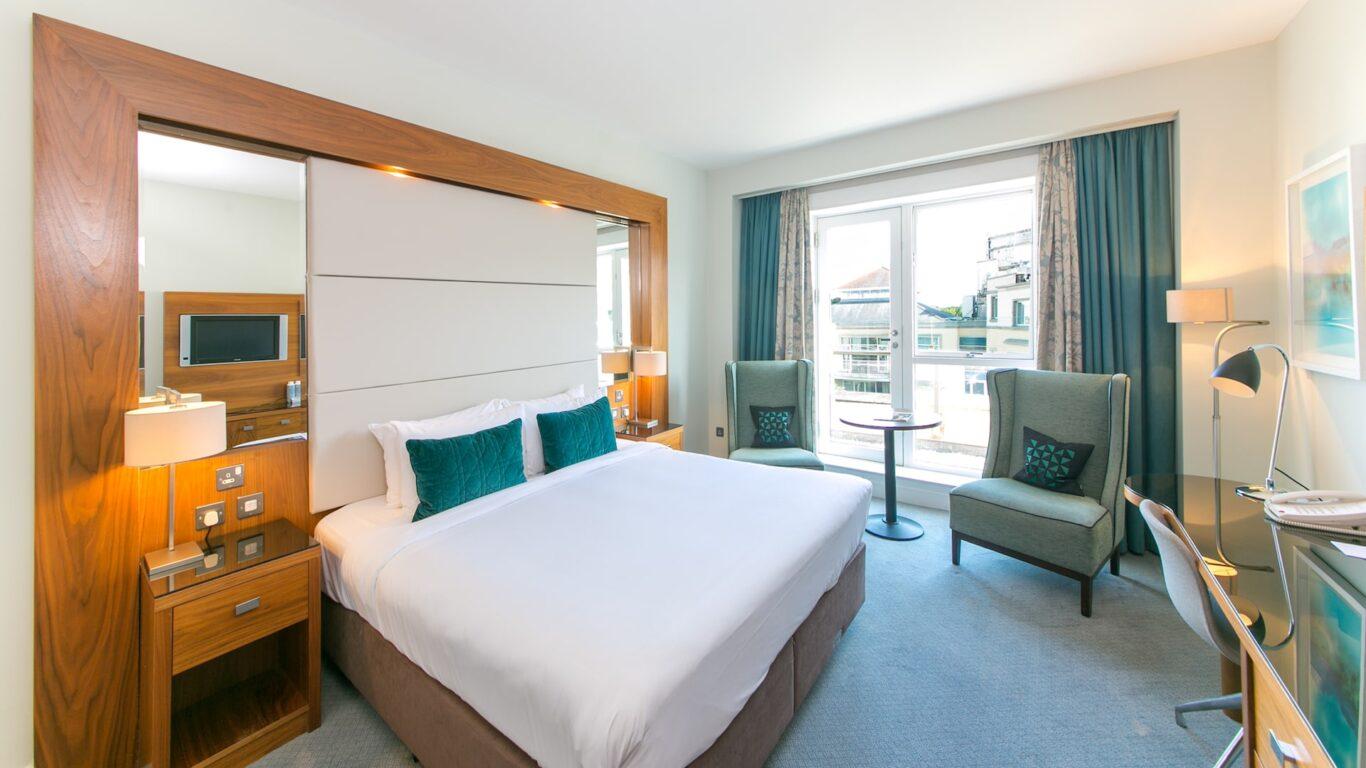 A bright hotel room with a double bed and cozy seating area.