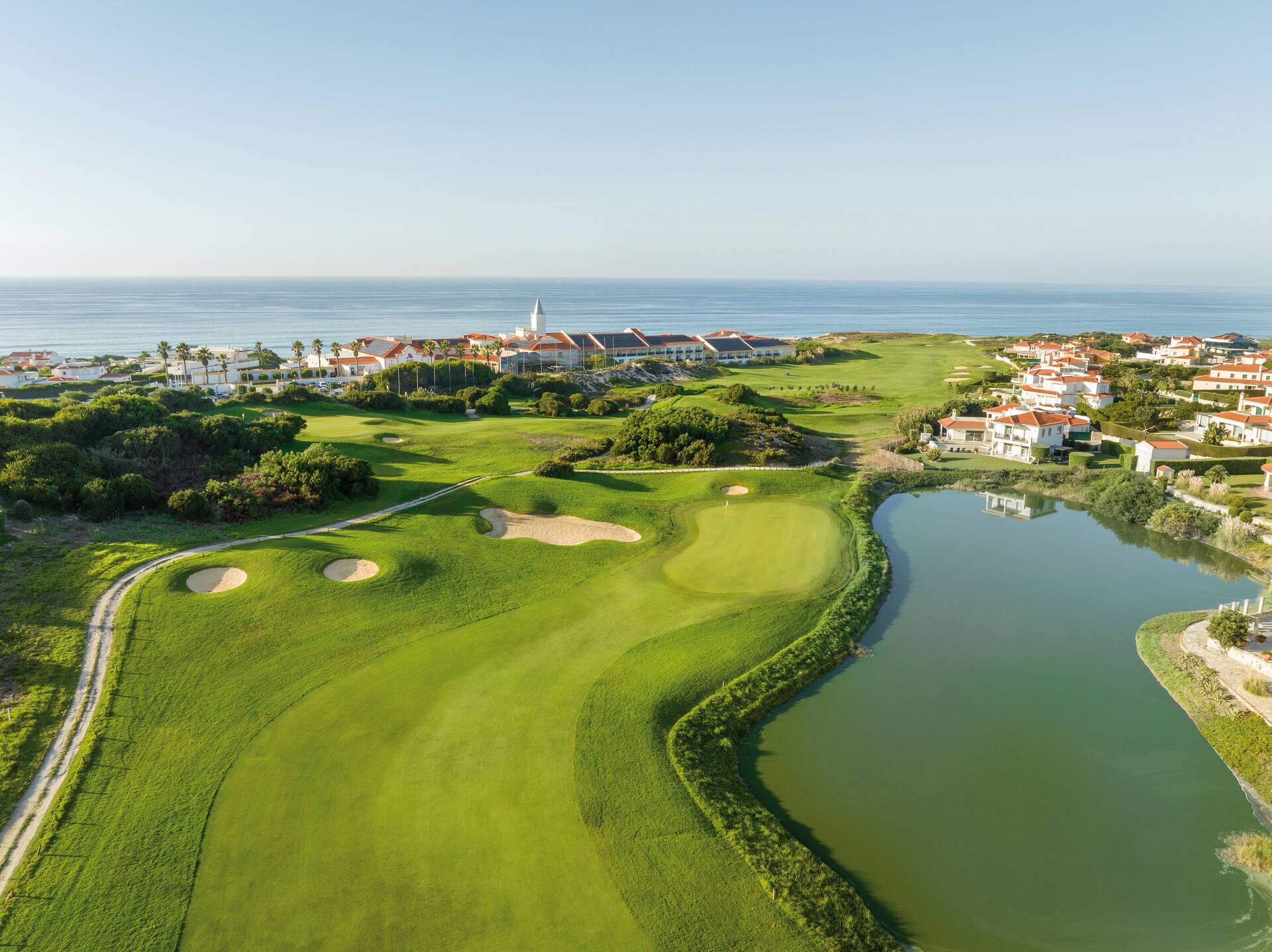 Aerial view of a winding fairway on the golf course with a water hazard on the right and Marriott Praia d'El Rey in the background