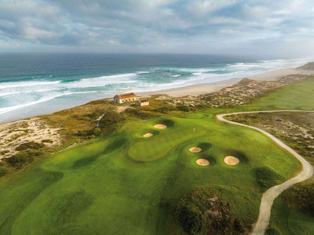 Aerial view of an undulating green with pot bunkers around it and the beach behind