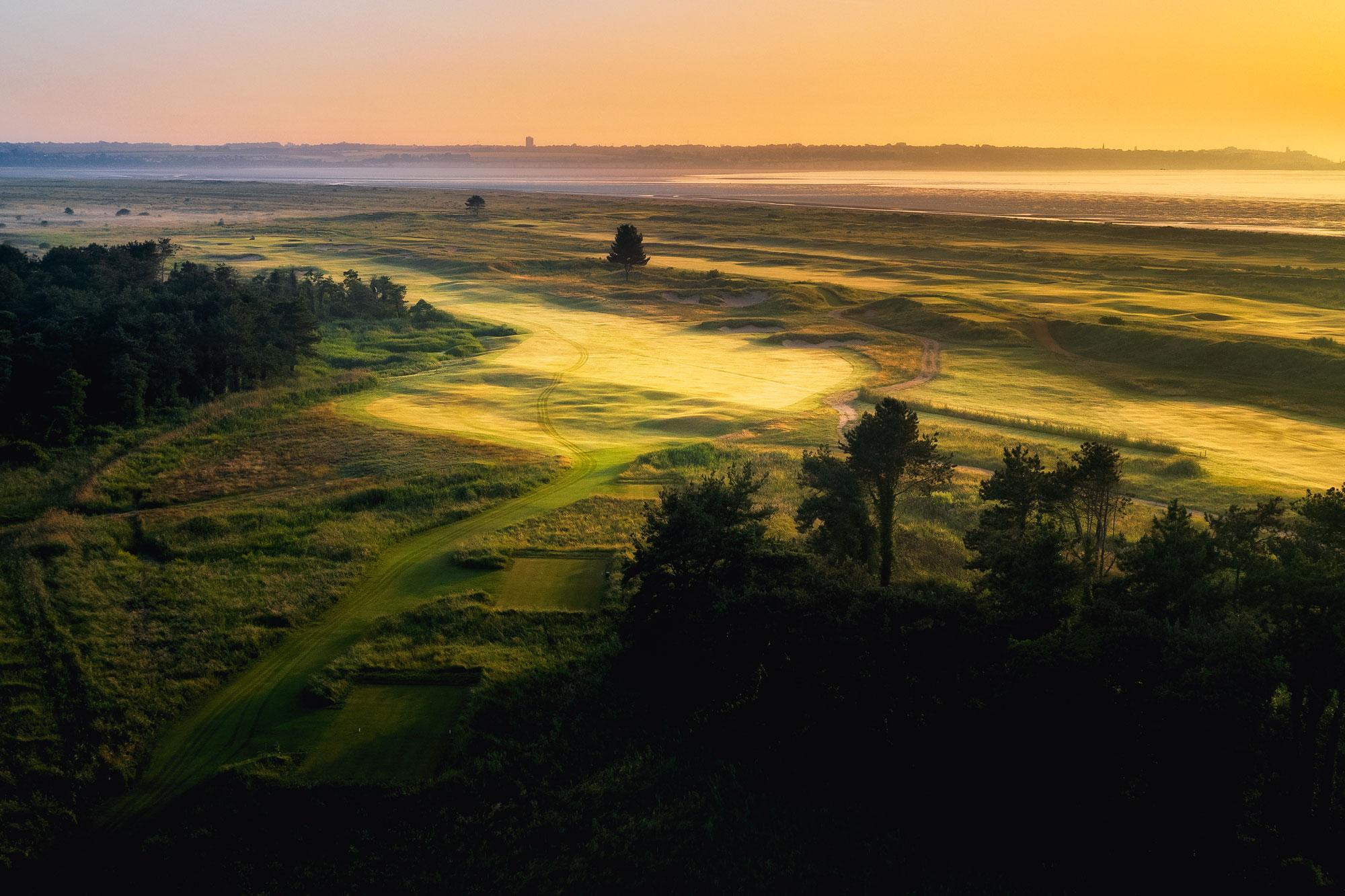 Coastal course framed by trees with sunlight illuminating the fairways.