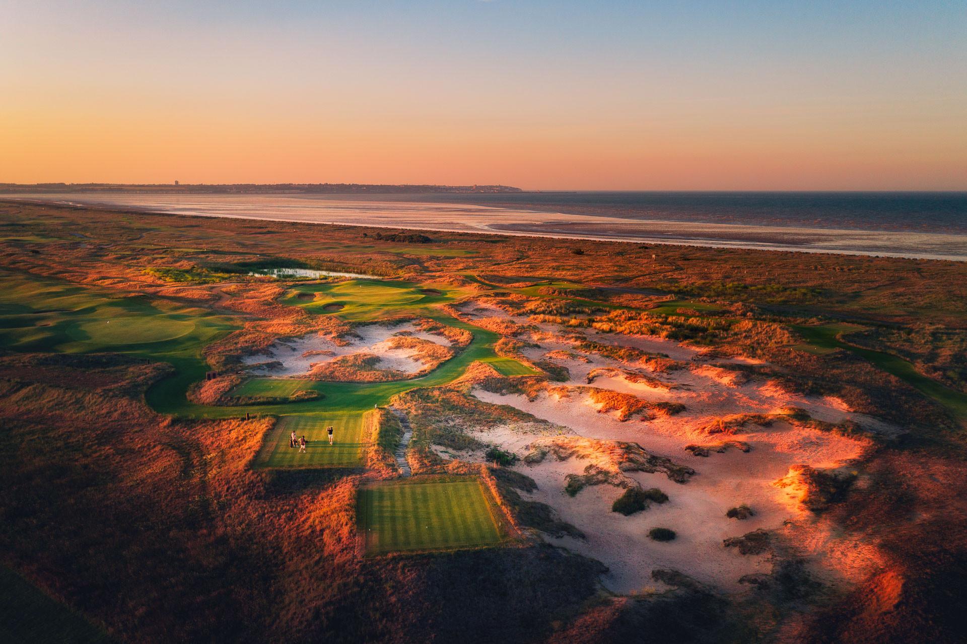 Dramatic sunset over a sandy, natural links layout by the ocean.